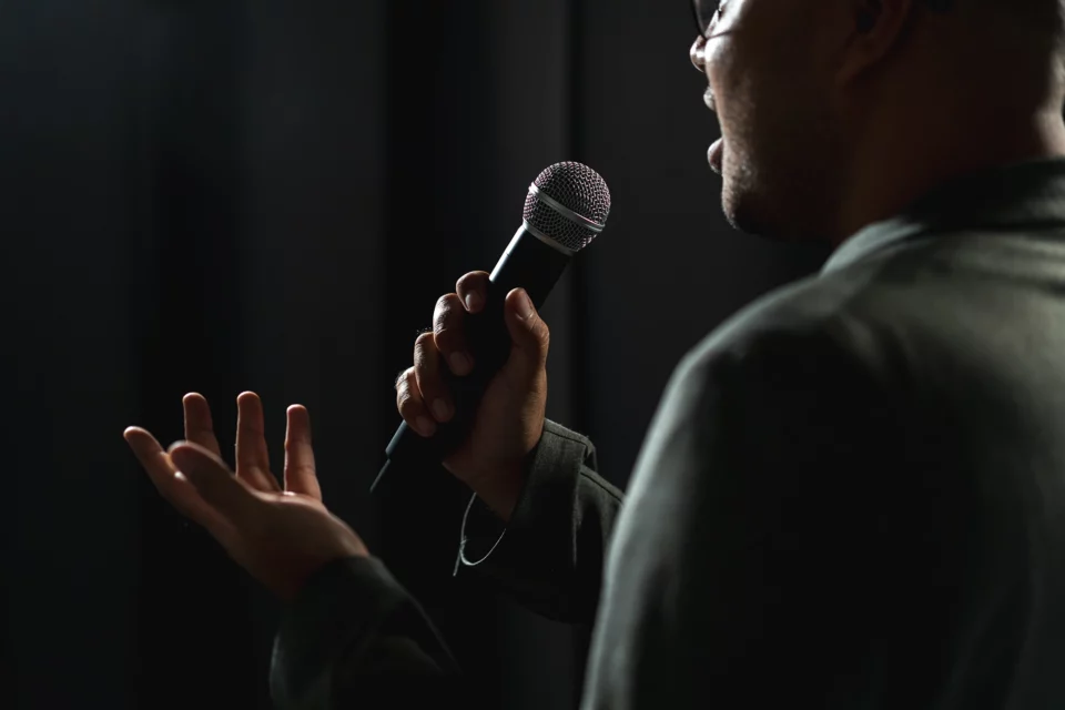 En mann holder en mikrofon foran en mørk bakgrunn.