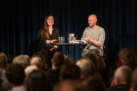 En mann og kvinne sitter ved et bord foran et publikum.