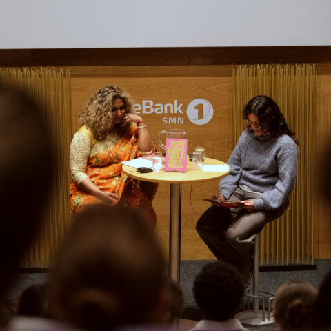 To personer deltok i en diskusjon på scenen, og satt ved et rundt bord med en bok med tittelen 