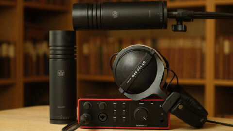 Et par studiomikrofoner, et par Beyerdynamic DT 770 Pro-hodetelefoner og et Focusrite Scarlett-lydgrensesnitt på et bord med bokhyller i bakgrunnen.