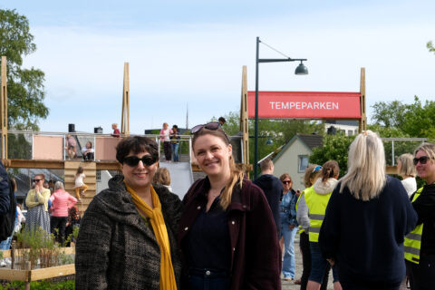 Tempe_Asieh_Nina, Foto: Kristian Lillenes/Litteraturhuset i Trondheim To kvinner står foran en folkemengde i Tempeparken, med mennesker samlet og sosialt samvær utendørs under en klar himmel.